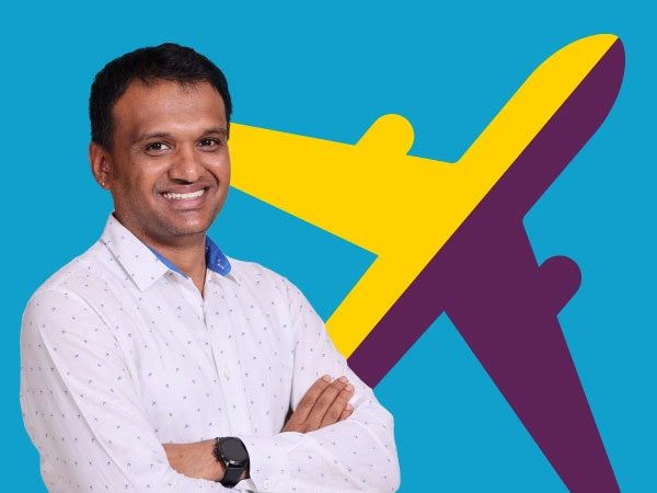 Smiling man in a white shirt with arms crossed, in front of a large yellow and purple airplane silhouette on a blue background.
