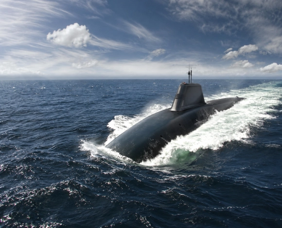 Submarine surfacing through ocean water, creating white wake against a blue sky with scattered clouds.