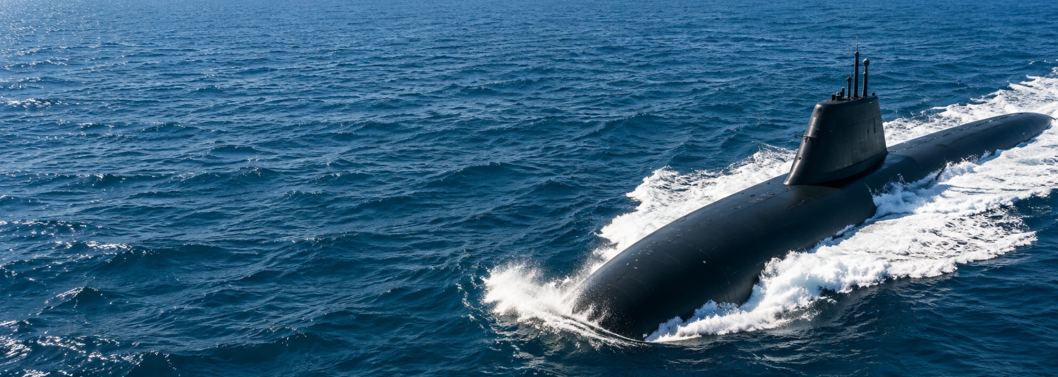 A dark submarine slicing through blue ocean waves, with its conning tower visible above water.