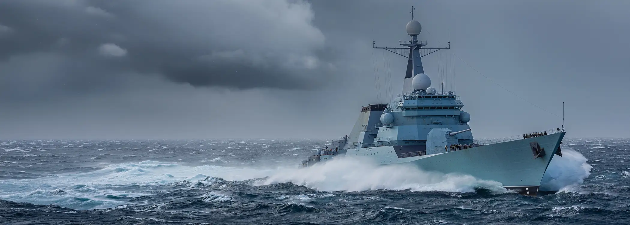 A gray military battleship cutting through rough ocean waves under dark storm clouds at sea. **(Informative)**