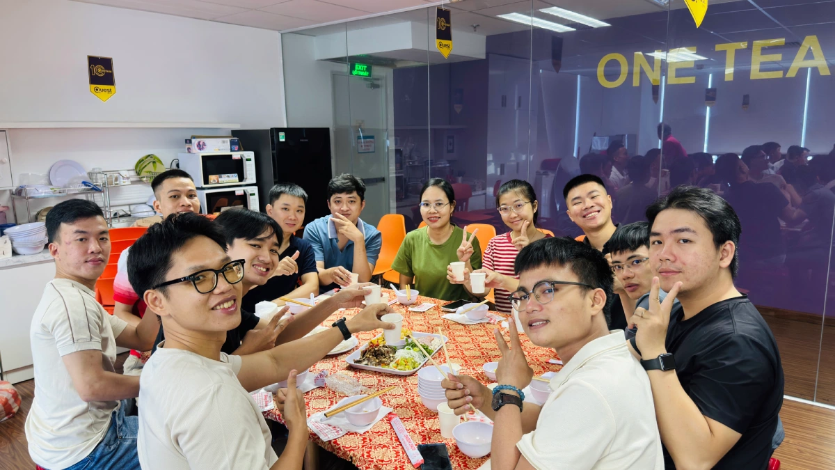 A group of twelve cheerful colleagues sitting around a circular table for an office social meal,
