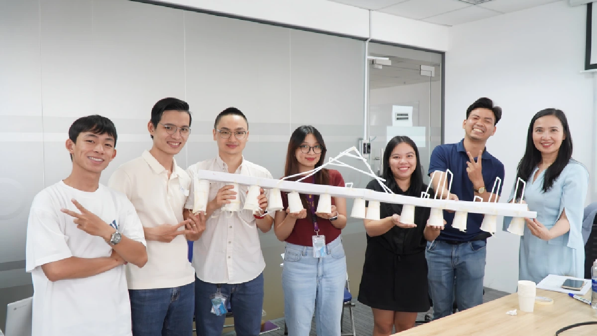 A group of people holding a handmade paper structure and smiling